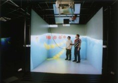 Two people standing inside a CAVE-style room-scale projection display, illustrating a world-grounded display.