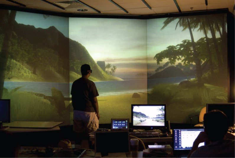 A person standing inside a three-wall surround-screen display showing a tropical beach scene.