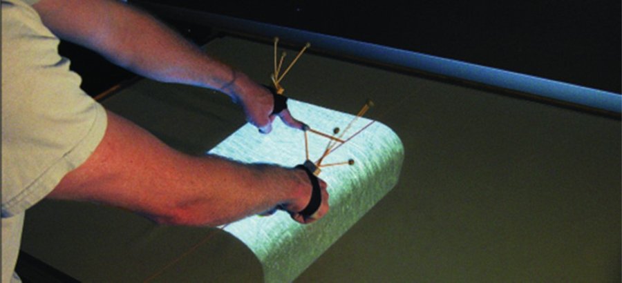 Hands wearing tracked gloves interacting with a 3D shape projected on a table-based workbench display.